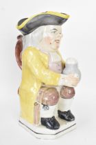 An early 19th century Toby jug, typically modelled seated resting a foaming mug of ale on one knee