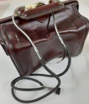 A late 20th Century maroon leather doctor's Gladstone bag with brass hardware and a stethoscope.