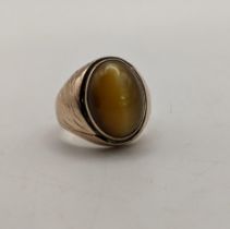 A yellow metal gents ring set with a cabouchon tiger's eye, engraved design to the shoulders,