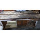 A wooden workbench with an iron vice to the right side, drawers and open storage spaces, on block