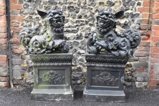 A pair of mid/late 20th century earthenware garden statues of Chinese foo dogs, both in a dark