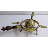 A brass plate warmer with turned wooden handle, resting on scrolled feet Location:
