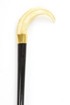 An Edwardian ebonised walking stick, with a warthog tusk handle, brass bound collar and a tapered