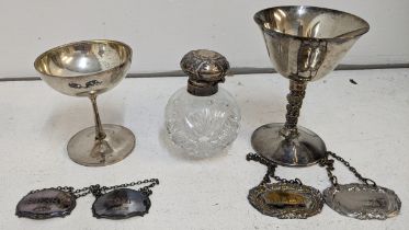 Silver to include a cup and two decanter labels, 125.5g, a silver top scent bottle and a silver