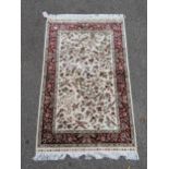 A Turkish silk rug decorated with exotic birds and flowers on a cream ground with a red border,