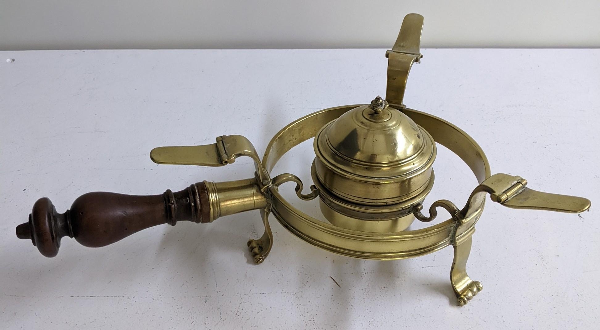 A brass plate warmer with turned wooden handle, resting on scrolled feet Location: 7-3 If there is