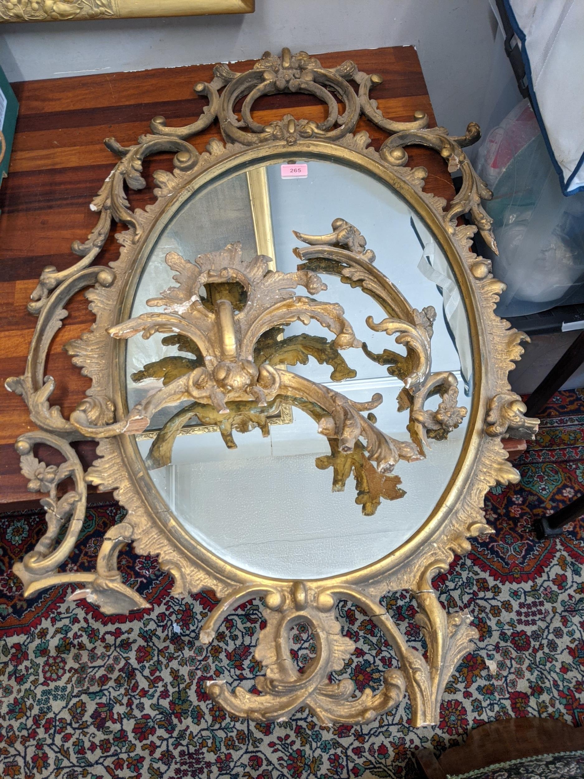 A late 19th /early 20th century oval gilt wall mirror ornately and symmetrically decorated in