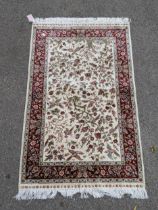 A Turkish silk rug decorated with exotic birds and flowers on a cream ground with a red border,