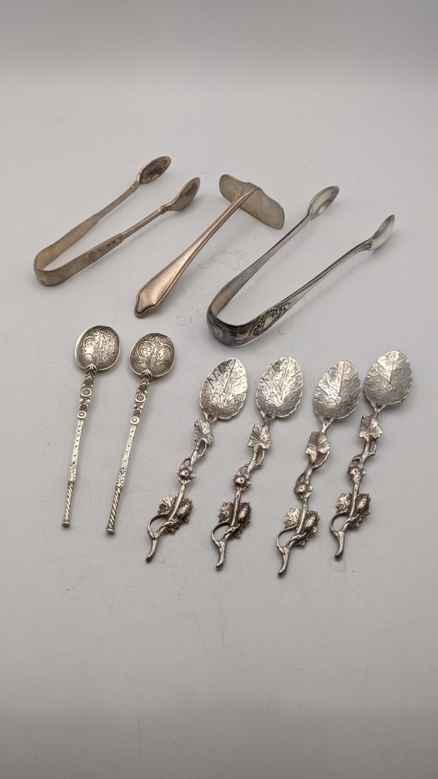 Two pairs of sugar tongs, a silver pusher, a pair of decorative coffee spoons and four white metal
