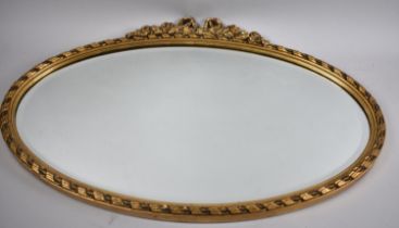 An Oval Gilt Framed Bevelled Glass Wall Mirror with Rose and Ribbon Finial, 72x48cm