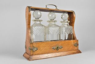 An Edwardian Oak and Silver Plate Mounted Three Bottle Tantalus, One Decanter Collar AF, 34cms Wide