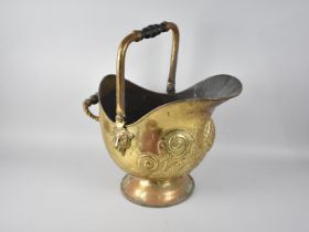 A Mid 20th Century Brass Helmet Shaped Coal Scuttle with Relief Decoration and Turned Wooden Handle,