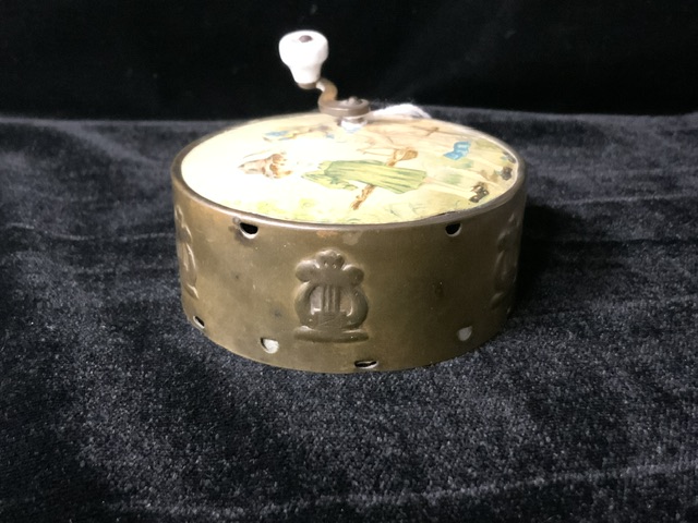 A VINTAGE CIRCULAR MUSIC BOX WITH TOP HANDLE DECORATED WITH A CHILDHOOD SCENE TO TOP; EMBOSSED HARPS - Image 3 of 3