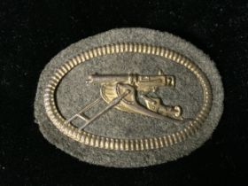 A WWI GERMAN MACHINE GUNNER PATCH / BADGE, OVAL FORM, METAL BORDER AND CENTRAL GUN