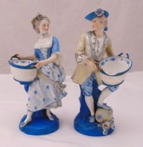 A pair of ceramic figurines of a man and lady in 18th century costume holding baskets, anchor mark