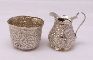An Indian white metal pear shaped cream jug profusely chased with flowers and leaves and a