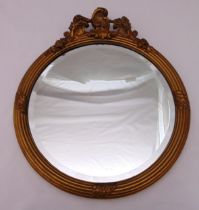 A gilded wooden circular wall mirror surmounted by stylised leaves, 46.5 x 40cm
