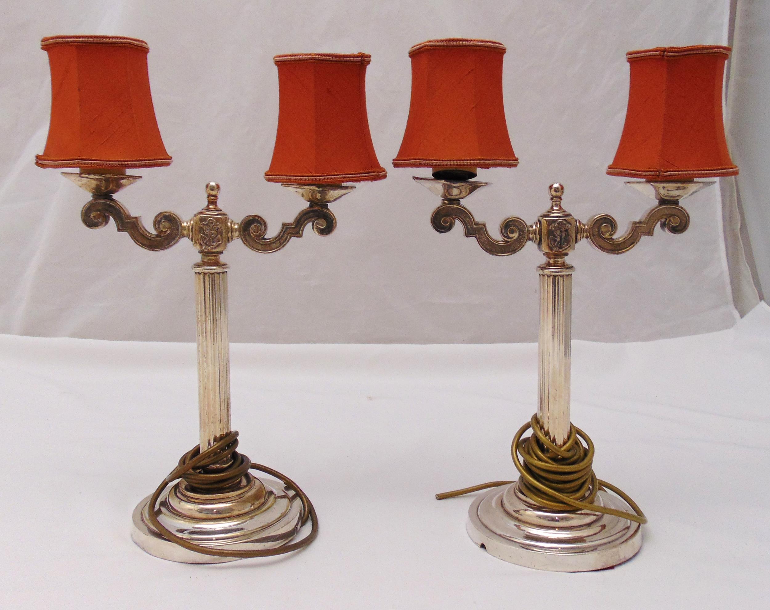 A pair of silver plated two branch table lamps with column supports on raised circular bases,