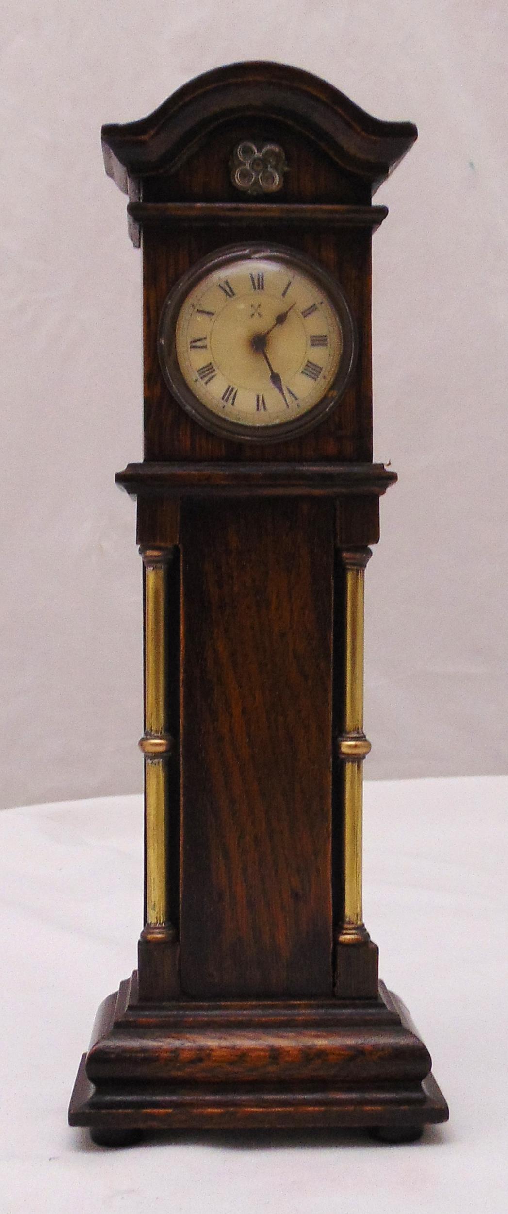 An Edwardian miniature oak cased grandfather clock with flanking brass columns on raised rectangular