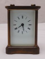 A brass carriage clock of customary form, white enamel dial with Roman numerals and carrying handle,