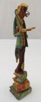 A painted wooden figurine of a man reading a book, on raised base in the form of three books, 32.5cm