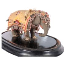 A miniature Indian elephant, with all over jewelled decoration, under a glass dome. H - 16cm.