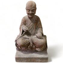 A large and impressive Chinese seated figure carved from a single block of stone, the figure holding