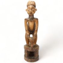 An early/mid 20th century Cameroon carving, of a chief on a stool with a bats head mask, height 65cm