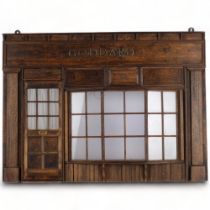 A wall-hanging stained wood ornamental shop front, with glazed window and door panels "Goddard",