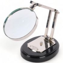 A reproduction silver plated adjustable desk magnifying glass, on plinth, 12.5cm diameter