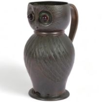 An Arts and Crafts copper owl jug, stylised form with red glass eyes and brass handle, H16cm,