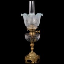 An Antique brass oil lamp, with coloured frilled edge shade and glass font on an embossed brass