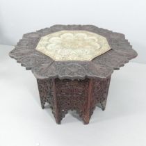 An Oriental octagonal occasional table on folding base, with brass insert and all-over carved and