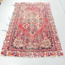 A red-ground Persian Sarouk rug. 220x135cm Heavily worn in places. Loss to edges and fringes.