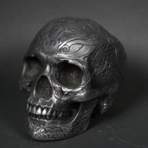 A cast composite sculpture of a human skull, embossed tribal decoration, with figures, birds and