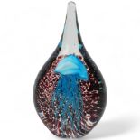 An elongated hand made glass paperweight, with internal blue jellyfish on spotted amethyst