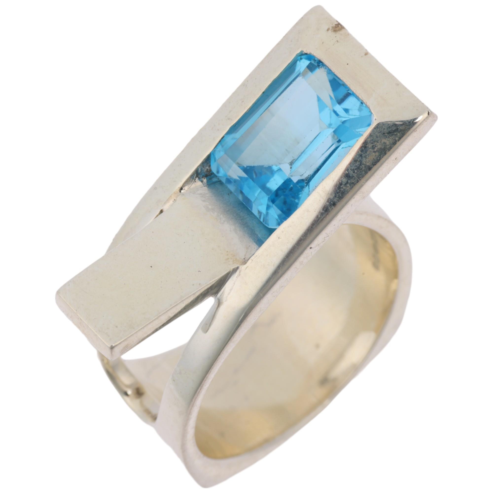 A modern sterling silver blue topaz crossover ring, London 2023, band width 11.4mm, size P, 13g