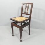 An Arts & Crafts mahogany Beethoven adjustable piano chair, with cane seat. Mechanism A/F. The