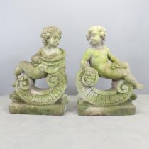 A pair of weathered composite cherub garden statues, the figures reclining on a scrolled base.