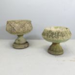 Two similar weathered concrete garden urns on stands, with acanthus leaf decoration. Largest