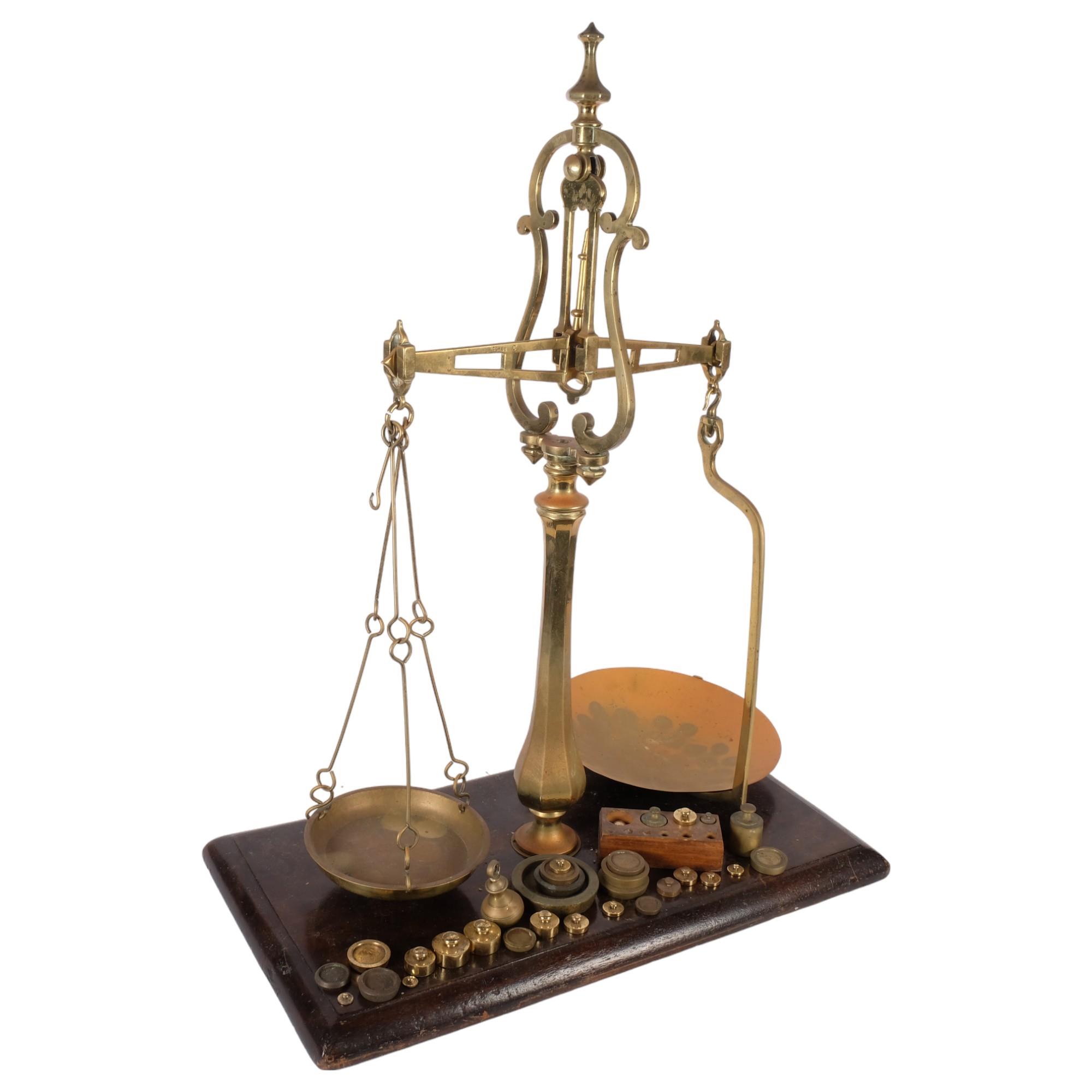 A large Antique brass balance scale and weights, on stained wood plinth, H77cm