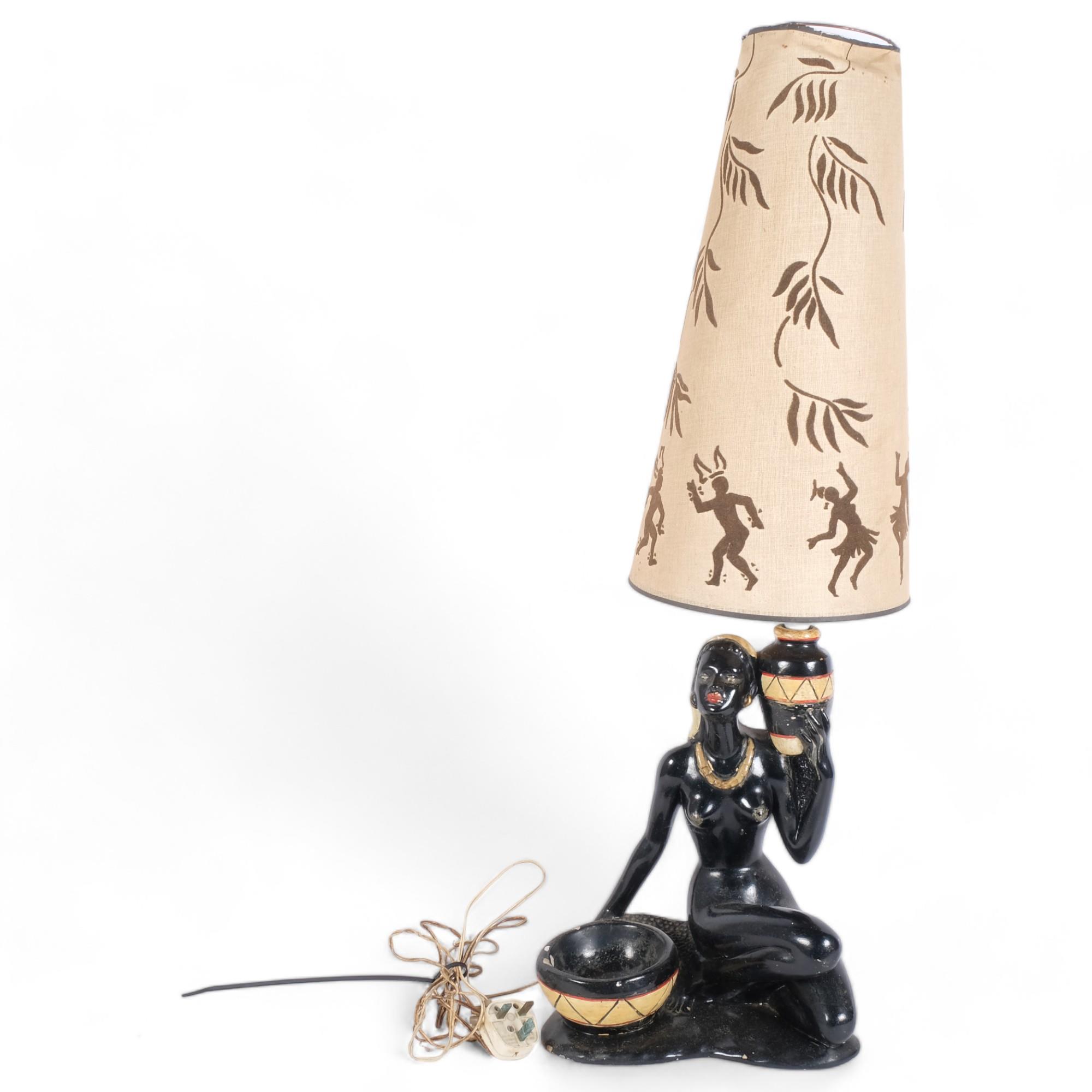 A painted plaster table lamp in the form of a Nubian style female figure, with associated shade,