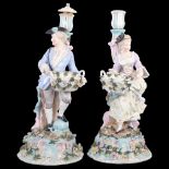 A pair of German porcelain candlesticks, supported by figures with bowls on flower-strewn plinths (