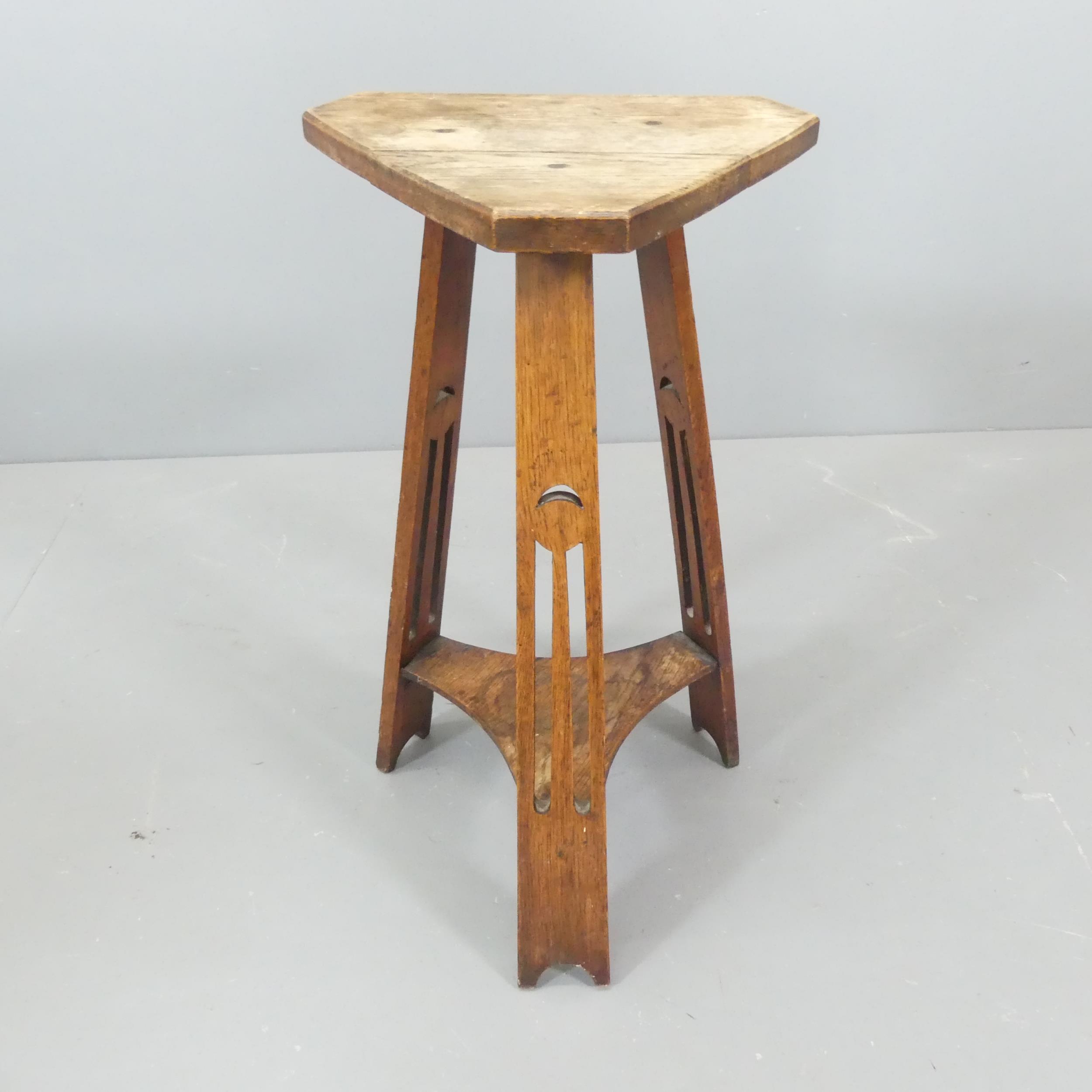 An Arts & Crafts oak triangular two-tier occasional table. Height 68cm.