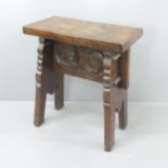 A continental elm stool of pegged construction, with carved face decoration. 51x58x28cm.
