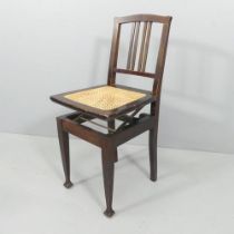 An Arts & Crafts mahogany Beethoven adjustable piano chair, with cane seat. Mechanism A/F. The