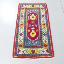 A red-ground tufted wool Kazak rug. 140x76cm.