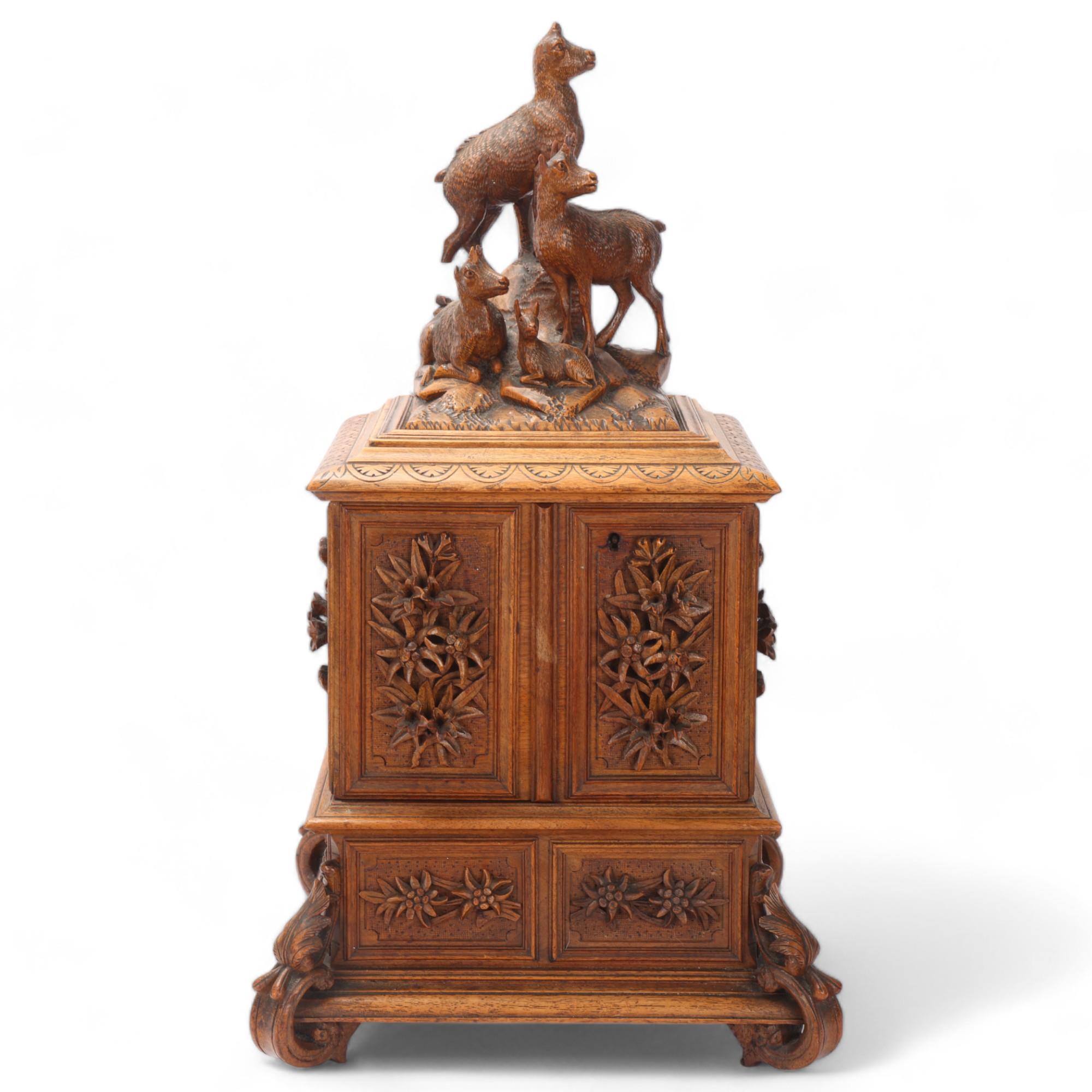 An ornate 19th century Black Forest table cabinet, the lid surmounted a carved wood group of deer, 2
