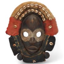 A Dan hardwood Tribal mask in cowrie shell and textile surround, height 31cm