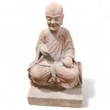 A large and impressive Chinese seated figure carved from a single block of stone, the figure holding